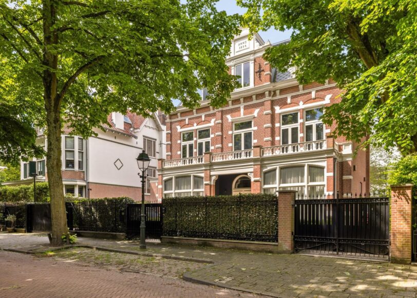 Vooraanzicht van een statig herenhuis aan de Parkweg 18, 2585 JK 's-Gravenhage, omgeven door hoge bomen en een smeedijzeren hek met een rustige, groene omgeving