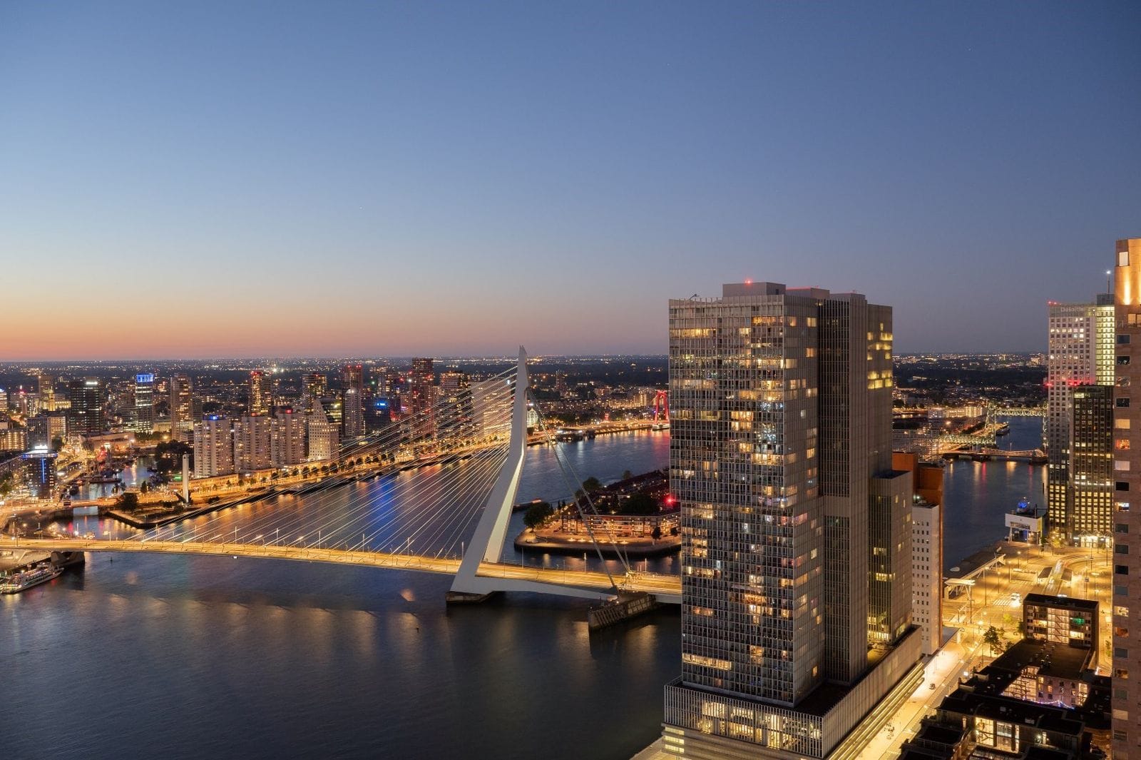 Prachtig uitzicht vanuit het Montevideo gebouw over de verlichte Erasmusbrug en de skyline van Rotterdam bij nacht, met moderne hoogbouw, de Maas, en een sfeervolle stadshorizon op de achtergrond.