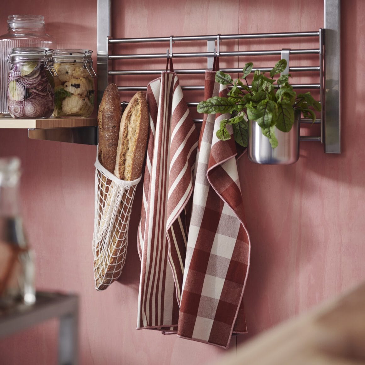 IKEA-wandrek met haken, kruidenplantje en keukendoeken tegen een zachte roze muur