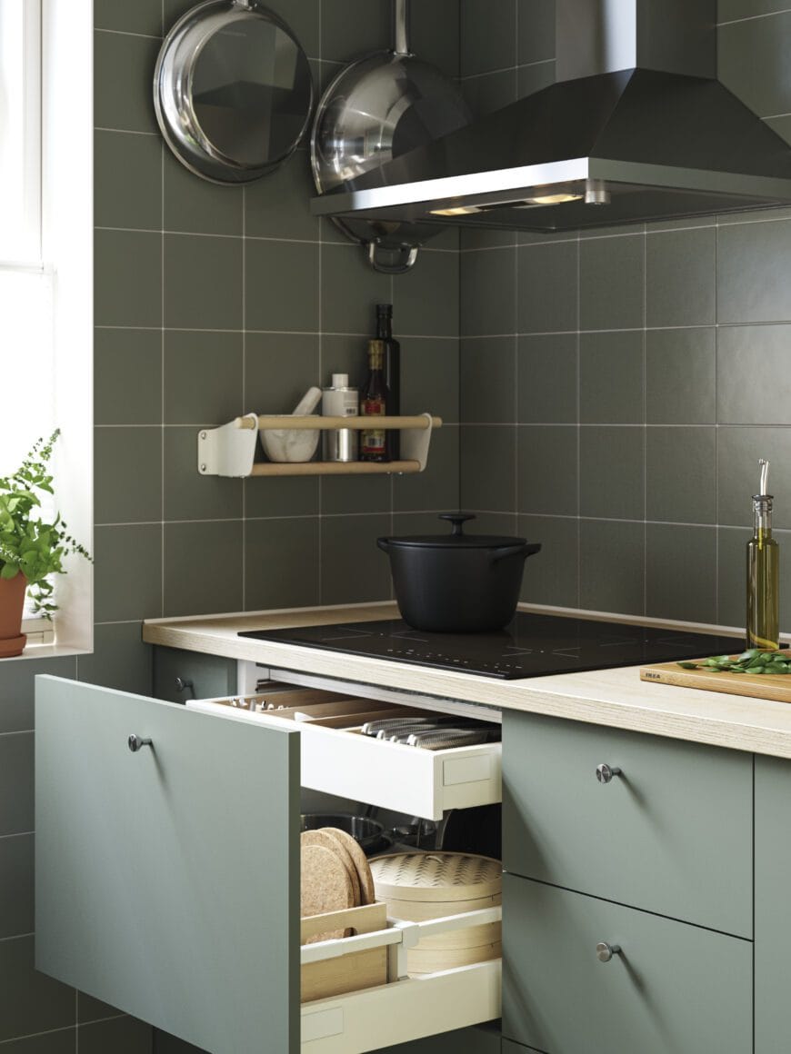 Moderne IKEA-keuken met afzuigkap boven een kookplaat en greeploze groene kastfronten.